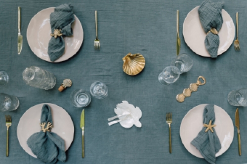 gedekte tafel met pastelgroene servetten en tafelkleed, goudkleurige messing servetringen, schaaltje en flesopener